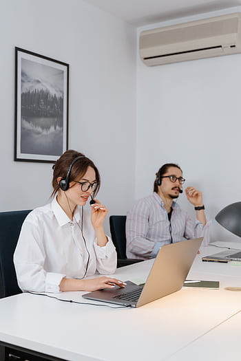 Two professionals working remotely in a modern office space, wearing headsets and using laptops. HD phone wallpaper