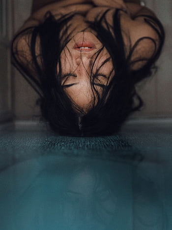 A striking portrait of a woman with long hair and a serene expression, reflected on a smooth surface. HD phone wallpaper