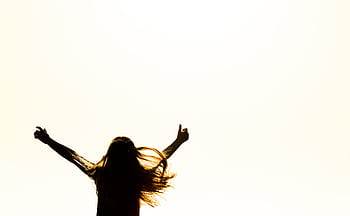 Backlit silhouette of a woman with arms up, capturing dom and joy in a minimalist setting. HD wallpaper