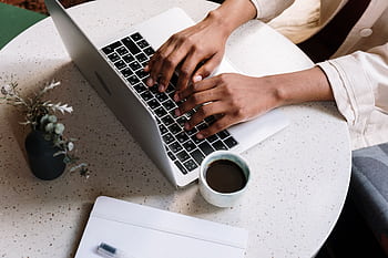A person typing on a laptop at a café table with coffee and a notebook. HD wallpaper