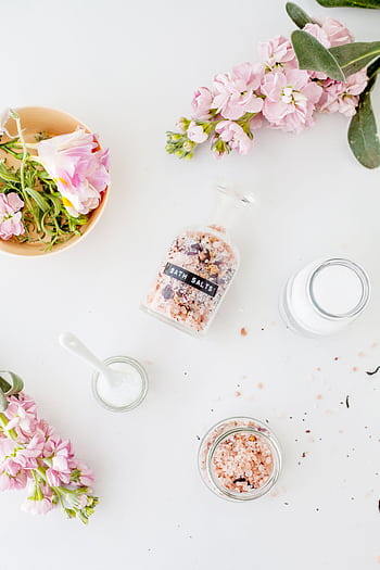 Flat lay of bath salts, pink flowers, and cosmetic containers on a white background. HD phone wallpaper