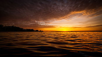 A stunning sunset over calm ocean waters with vibrant colors and dramatic clouds. HD wallpaper