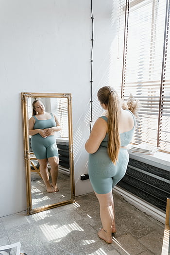 Confident plus size woman in activewear looking at her reflection, embracing body positivity. HD phone wallpaper