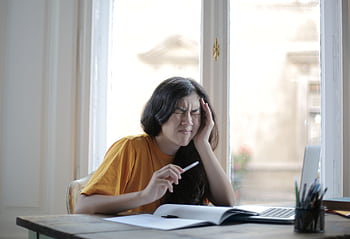 Young woman in distress, suffering from headache while working at home desk with laptop and notebook. HD wallpaper