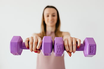 A woman confidently holds purple dumbbells, focusing on fitness and strength, in a studio setting. HD wallpaper