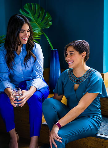 Two women enjoying a lively conversation indoors, showcasing stylish and colorful attire. HD phone wallpaper