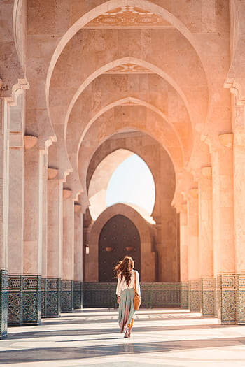 A woman walks through the stunning arches of Hassan II Mosque, Casablanca, highlighting Islamic architecture. HD phone wallpaper
