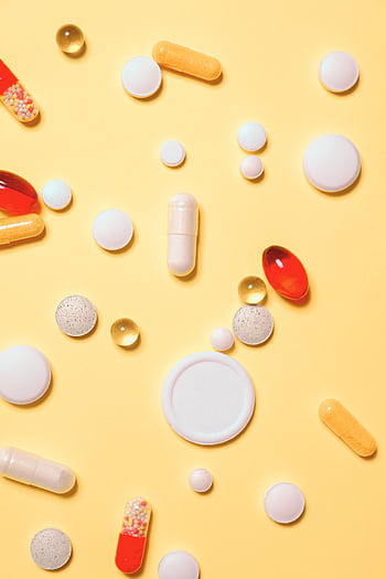 Colorful assortment of pills and capsules on a vibrant yellow background. HD phone wallpaper