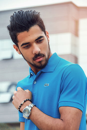 Portrait of a stylish adult male in a blue polo shirt, showcasing modern accessories, set against an urban background. HD phone wallpaper
