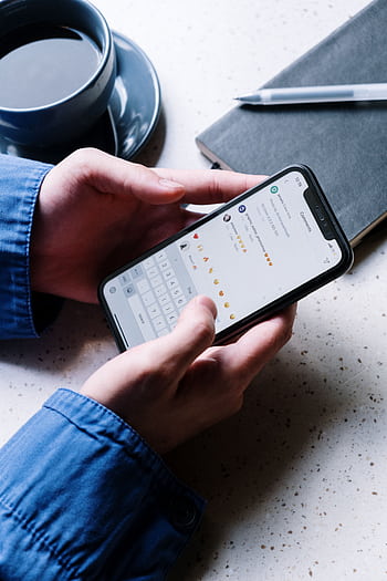 Close-up of hands holding smart, using chat app. Coffee and notebook nearby indicate casual setting. HD phone wallpaper