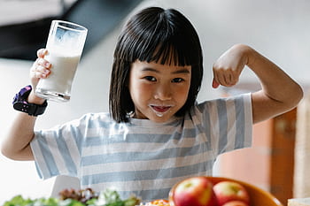A happy child drinking milk and flexing muscles, promoting a healthy breakfast habit. HD wallpaper
