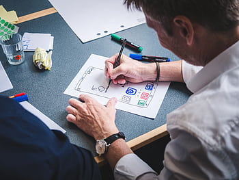 A designer sketches a mobile app prototype on paper at an office desk, focusing on creativity and design. HD wallpaper