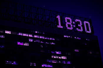 A modern building is illuminated at night with a prominent digital clock showing 18:30. HD wallpaper