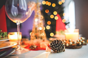 A warm and inviting Christmas table setting with candles, pinecones, and a wine glass. HD wallpaper