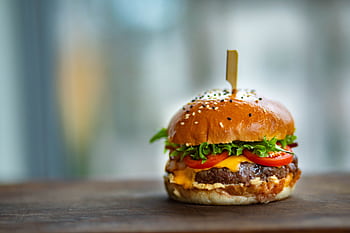 Mouthwatering cheeseburger with fresh tomatoes and lettuce on a wooden surface. HD wallpaper