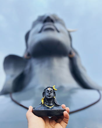 Close-up of a hand-held Adiyogi figurine against the monumental statue in Coimbatore. HD phone wallpaper