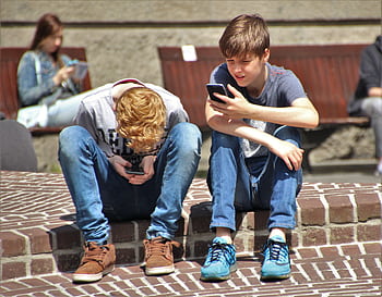 Two teenagers seated outdoors, focused on their smarts, embracing modern technology. HD wallpaper