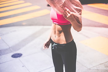 Athletic woman in pink activewear showing toned abs in urban San Francisco setting. HD wallpaper