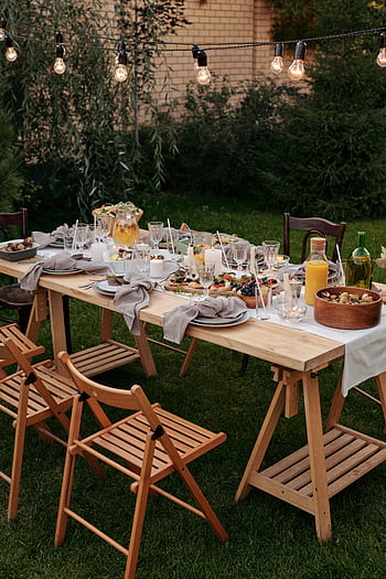 Charming outdoor dining setup with string lights and delicious meals set on a table. HD phone wallpaper