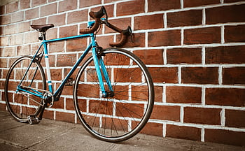 A classic blue racing bicycle parked against a rustic brick wall. HD wallpaper