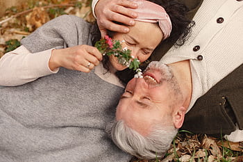 Senior couple lying on grass, smiling with affection, in a warm autumn setting. HD wallpaper