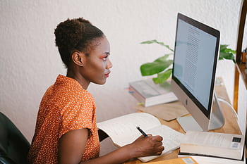A focused young woman studying with books and a computer at her home office desk. HD wallpaper