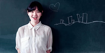Smiling young woman stands confidently by a blackboard with chalk drawings. HD wallpaper