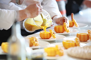 Chef performing culinary artistry by pouring vibrant pumpkin soup in decorative pumpkins. HD wallpaper