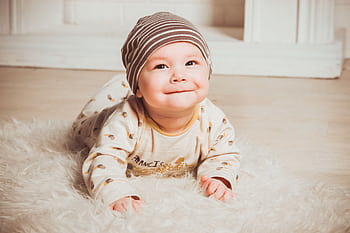 Charming baby smiling while lying indoors on soft rug wearing cozy outfit. HD wallpaper