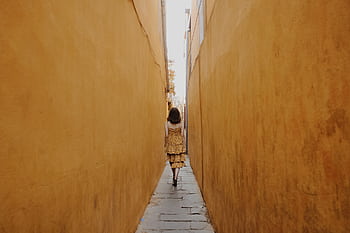 A woman in a yellow dress walks through a narrow alleyway with yellow walls in Hội An, Vietnam. HD wallpaper