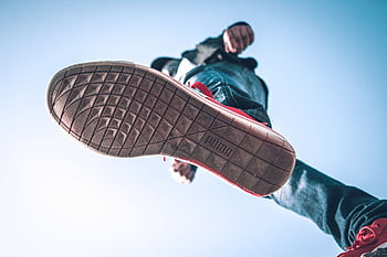 Low angle view of person wearing sneakers with focus on the sole against blue sky. HD wallpaper