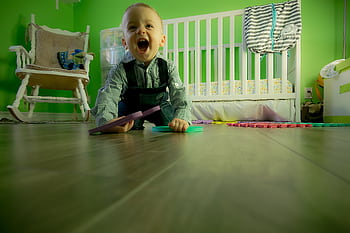 Delightful baby boy crawling on a wooden floor, playing happily in a vibrant green nursery. HD wallpaper
