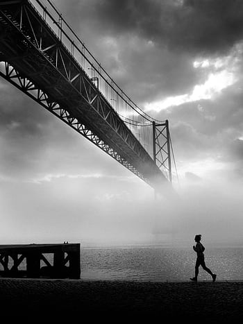 Silhouette of a person jogging near a misty river with a suspension bridge in the background. HD phone wallpaper