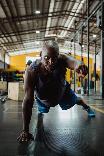 Muscular man demonstrating strength with a one-arm push-up in a gym. HD phone wallpaper