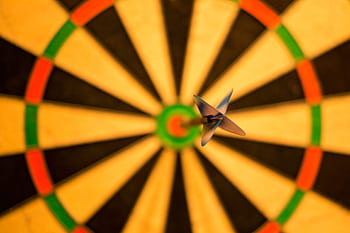 A close-up of a dart perfectly hitting the bullseye on a dartboard, symbolizing accuracy. HD wallpaper