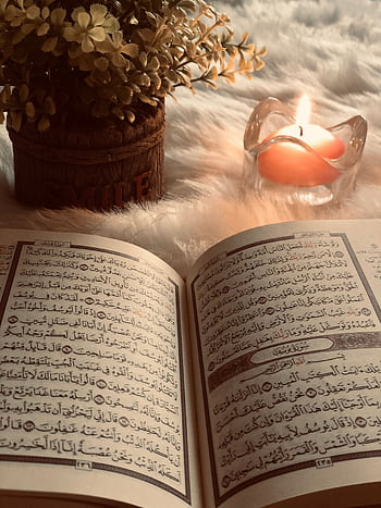 A Quran open to Surah An-Nur, with candlelight ambiance and decorative flowers. HD phone wallpaper