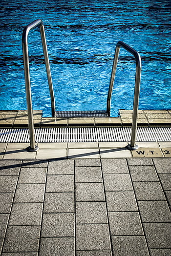 Close-up of a pool ladder with blue water, showcasing a serene outdoor setting. HD phone wallpaper