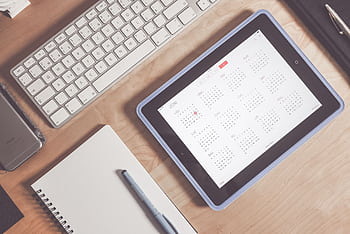 A tidy desk setup featuring a tablet displaying a calendar, keyboard, and stationary items. HD wallpaper