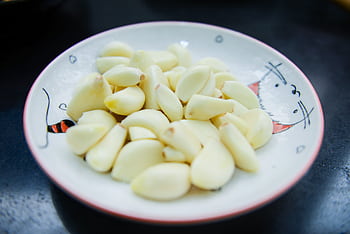 A close-up of peeled garlic cloves arranged on a decorative plate, highlighting their freshness. HD wallpaper