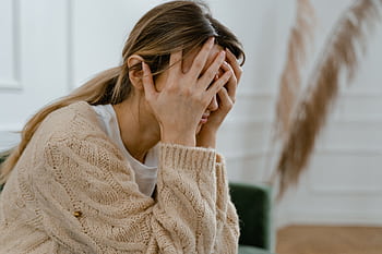 A woman sitting indoors covering her face in frustration, depicting stress and mental health challenges. HD wallpaper