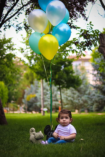 Cute baby sitting on grass with colorful balloons in a scenic park setting. HD phone wallpaper