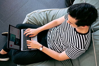 A man in a striped shirt using a laptop on a bean bag, embodying relaxed productivity. HD wallpaper