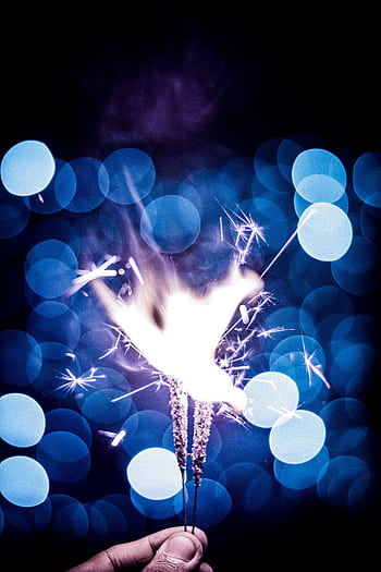 Close-up of sparkler against bokeh lights background, embodying celebration and cheer. HD phone wallpaper