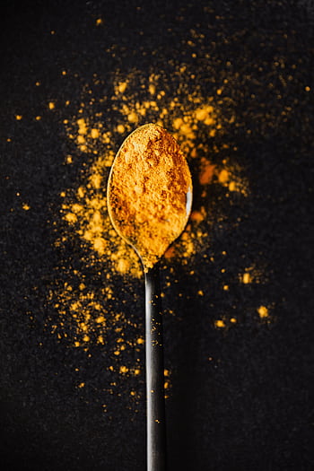 Top view of turmeric powder on a spoon against a dark background, showcasing vibrant color and texture. HD phone wallpaper