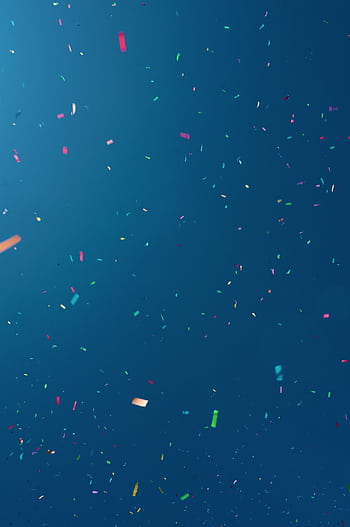 Colorful confetti pieces falling against a bright blue background, perfect for festive celebrations. HD phone wallpaper
