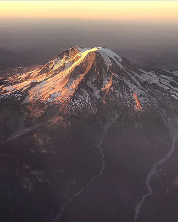 Stunning aerial view of a snowcapped mountain in soft dawn light, showcasing nature's beauty. HD phone wallpaper