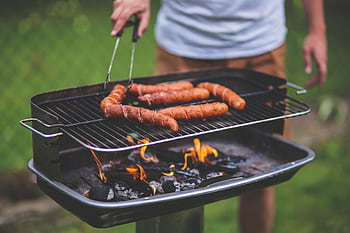 Man grilling sausages on an outdoor barbecue with flames and charcoal. HD wallpaper