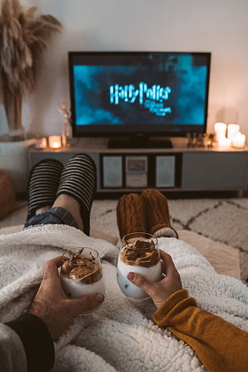 A couple enjoys a cozy movie night with drinks, wrapped in blankets, watching a Harry Potter film on TV. HD phone wallpaper