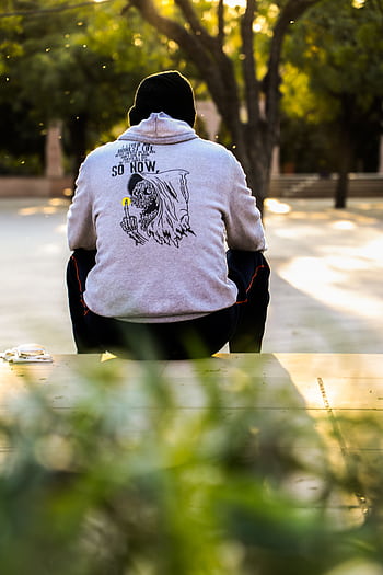Person wearing a hoodie sitting outdoors in a sunny park, capturing a moment of relaxation. HD phone wallpaper