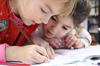 Two young girls focus on a drawing project together, sharing creativity and learning. HD wallpaper